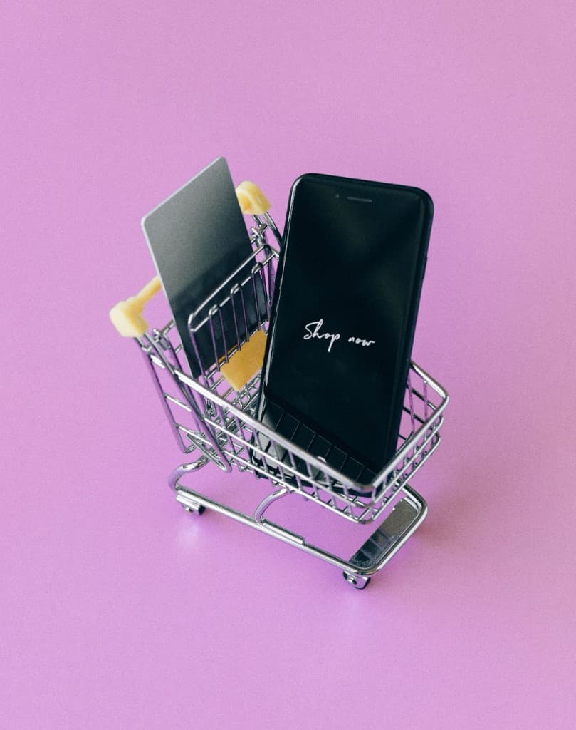 Miniature shopping cart with a smartphone and credit card on a purple background